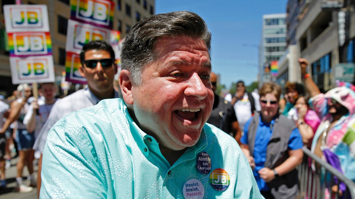 Illinois Gov. J.B Pritzker smiles and shakes hands in a dress shirt at a rally