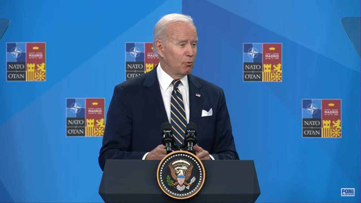 Joe Biden, in a suit with a striped tie, speaks before a NATO logo behind the presidential seal