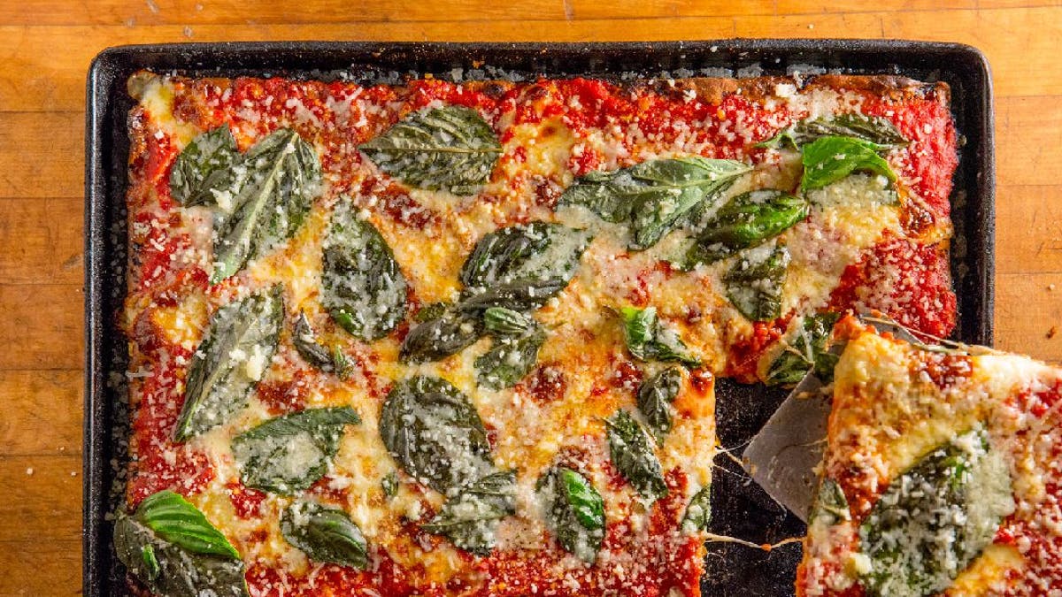 A well-done pizza with tomato sauce, cheese and basil is being served from a roasting pan.