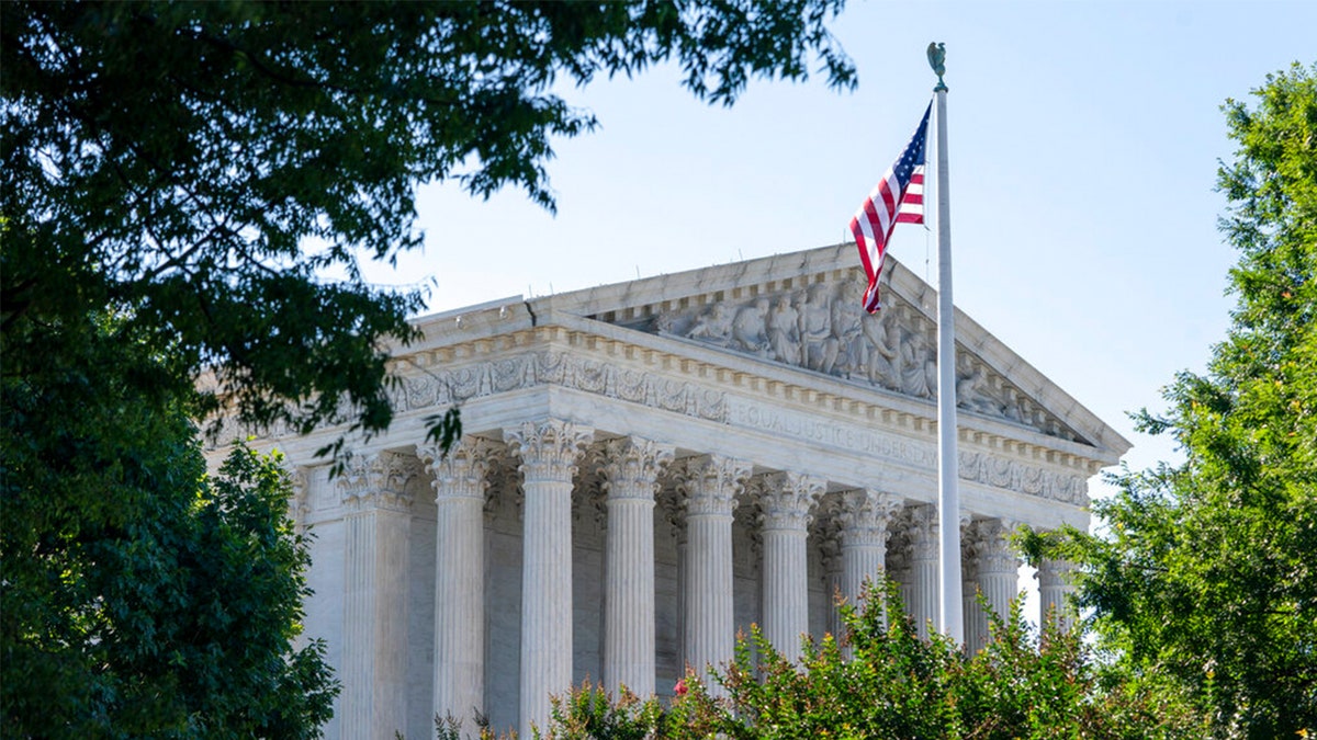 US Supreme Court building framed by trees, US flag in front