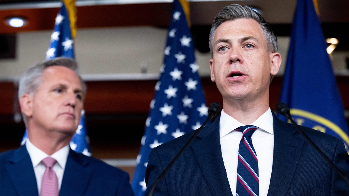 Rep. Jim Banks in a blue suit speaking next to Kevin McCarthy