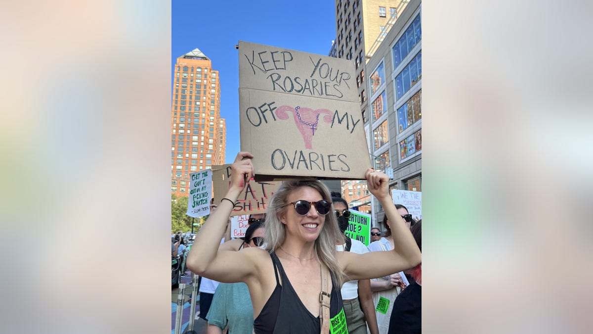 A woman holds a sign reading, "Keep Your Rosaries Off My Ovaries"