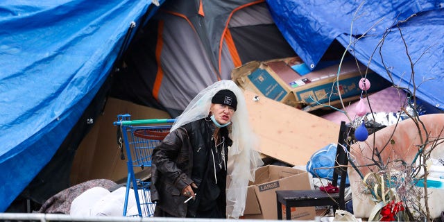 A homeless woman wearing a veil stands near a tent pitched by Echo Park Lake.