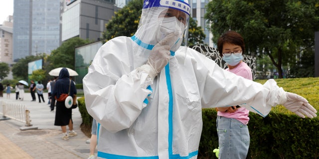 A worker wearing personal protective equipment (PPE) walks next to people lining up to get tested at a mobile nucleic acid testing site amid the coronavirus disease (COVID-19) outbreak in Beijing, China June 10, 2022. 