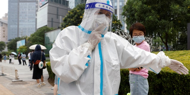 A worker wearing personal protective equipment (PPE) walks next to people lining up to get tested at a mobile nucleic acid testing site amid the coronavirus disease (COVID-19) outbreak in Beijing, China June 10, 2022. 