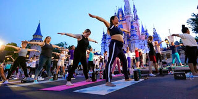 Nearly 2,000 cast members practice sunrise yoga in front of Cinderella Castle at Walt Disney World, June 21, 2022, in Lake Buena Vista, Florida. (AP Photo/John Raoux)