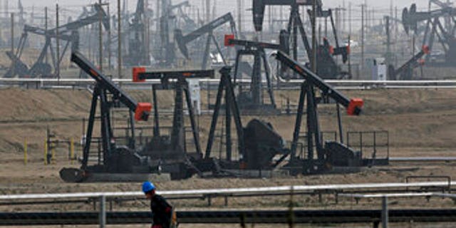 A worker walks past pump jacks operating at the Kern River Oil Field in Bakersfield, California.