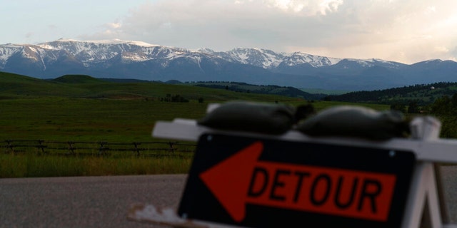 Snow-capped mountains loom in the background as a detour sign directs traffic off a road damaged by severe flooding in Fishtail, Montana, Friday, June 17, 2022. 