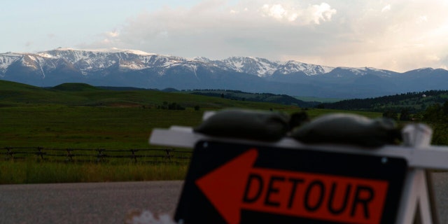 Snow-capped mountains stand in the background as a detour sign directs traffic off a damaged road from severe flooding in Fishtail, Mont., Friday, June 17, 2022. 