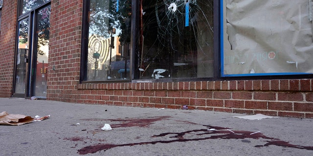 Blood is seen at the scene of a fatal overnight shooting on South Street in Philadelphia, Sunday, June 5, 2022, where bullet holes on a storefront window from a prior shooting can also be seen. 