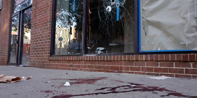 Blood is seen at the scene of a fatal overnight shooting on South Street in Philadelphia, Sunday, June 5, 2022, where bullet holes on a storefront window from a prior shooting can also be seen. 