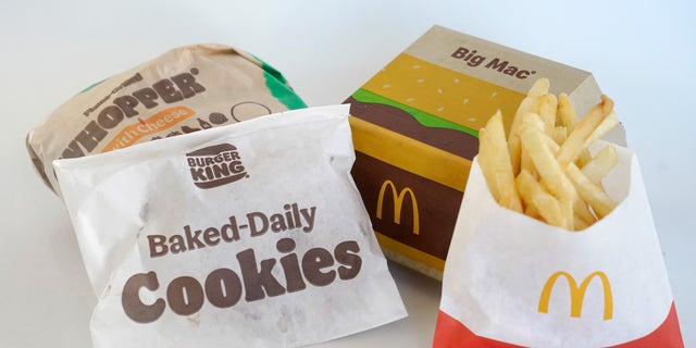 A Burger King Whopper in a wrapper, behind left, and a bag of Burger King cookies, left, rest next to a McDonald's Big Mac in a container, behind right, and a bag of McDonald's fries, in Walpole, Mass., Wednesday, April 20, 2022. Environmental and health groups are pushing dozens of fast food companies, supermarkets chains and other retail outlets to remove PFAS from their packaging. 