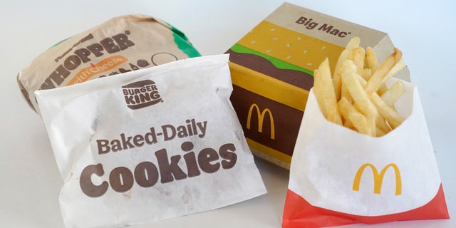 A Burger King Whopper in a wrapper, behind left, and a bag of Burger King cookies, left, rest next to a McDonald's Big Mac in a container, behind right, and a bag of McDonald's fries, in Walpole, Mass., Wednesday, April 20, 2022. Environmental and health groups are pushing dozens of fast food companies, supermarkets chains and other retail outlets to remove PFAS from their packaging. 