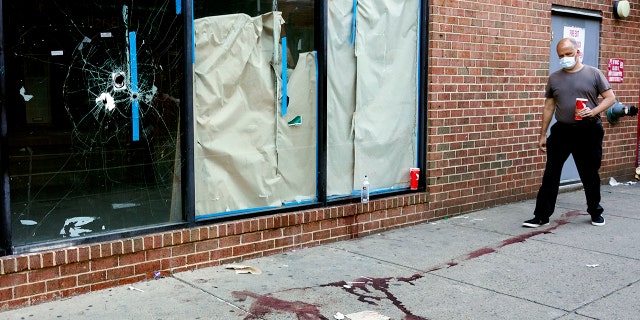 A person walks past the scene of a fatal overnight shooting on South Street in Philadelphia, Sunday, June 5, 2022, where bullet holes on a storefront window from a prior shooting can be seen.