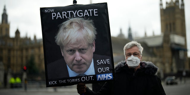 An anti-Conservative Party protester holds a placard with an image of British Prime Minister Boris Johnson, including the words "Now Partygate" with a backdrop of the Houses of Parliament, in London Dec. 8, 2021. 