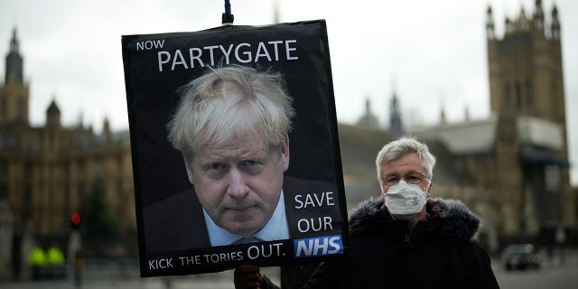 An anti-Conservative Party protester holds a placard with an image of British Prime Minister Boris Johnson, including the words "Now Partygate" with a backdrop of the Houses of Parliament, in London Dec. 8, 2021. 