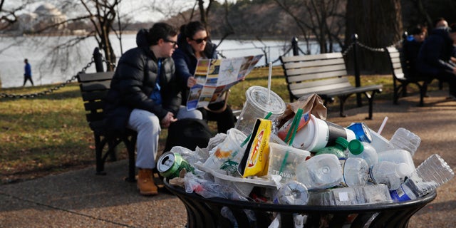 A trash can overflows as people sit outside of the Martin Luther King Jr. Memorial by the Tidal Basin in Washington, D.C., in December 2018.