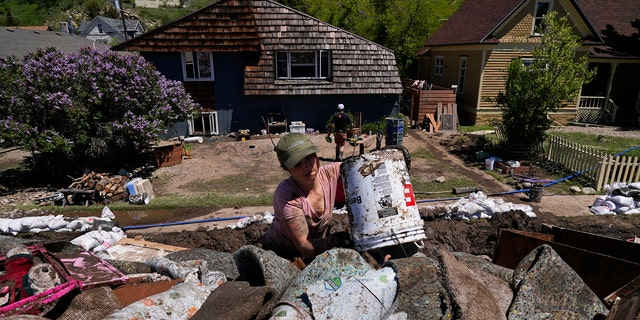 Alecia Halona dumps a bucket of debris into a trailer Wednesday, June 15, 2022, in Red Lodge, Mont. She responded to an online posting requesting help to clean out houses on a street that flooded when torrential rains swelled waterways across the Yellowstone region. 