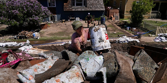 Alecia Halona dumps a bucket of debris into a trailer Wednesday, June 15, 2022, in Red Lodge, Mont. She responded to an online posting requesting help to clean out houses on a street that flooded when torrential rains swelled waterways across the Yellowstone region. 