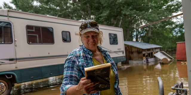 Lindi O'Brien picks up a commendation plaque to her father's police service from the barn of her parent's home badly damaged by the severe flooding in Fromberg, Mont., Friday, June 17, 2022. (AP Photo/David Goldman)