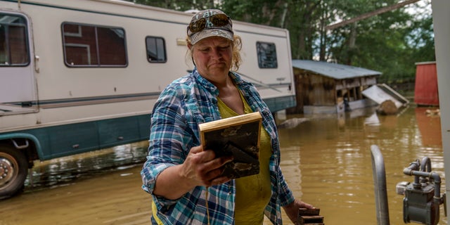 Lindi O'Brien picks up a commendation plaque to her father's police service from the barn of her parent's home badly damaged by the severe flooding in Fromberg, Mont., Friday, June 17, 2022. (WHD Photo/David Goldman)