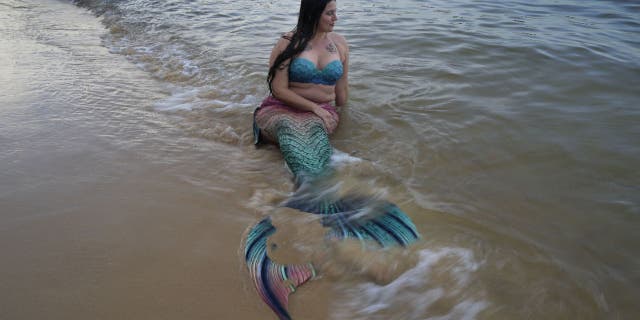 In this May 26, 2022, photo, Lauren Metzler, founder of Sydney Mermaids, sits on the shoreline of Manly Cove Beach in Sydney, Australia.