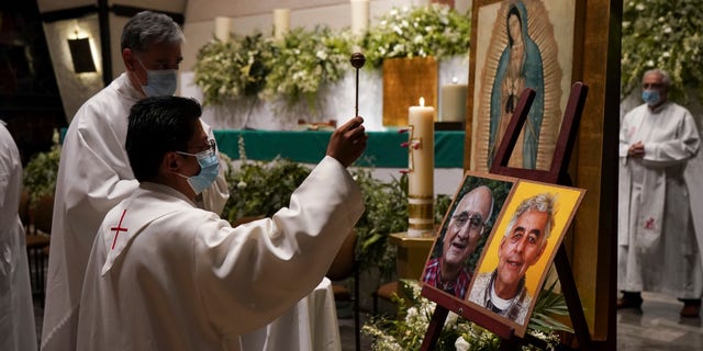A priest blesses the photos of the two Jesuit priests who were killed by crime boss.