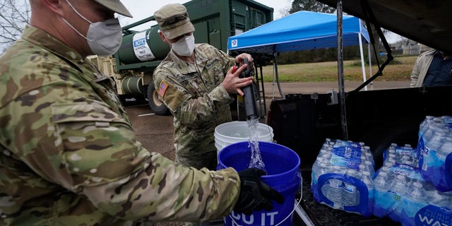 Mississippi Army National Guard Sgt. Chase Toussaint, right, and Staff Sgt. Matthew Riley, both with the Maneuver Area Training Equipment Site of Camp Shelby, fill 5-gallon buckets in March 2021 at a Jackson water distribution site. 