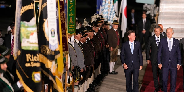 U.S. President Joe Biden, right, waves as he walks past Bavarian mountain riflemen and traditional costumers after his arrival at Franz-Josef-Strauss Airport near Munich, Germany, Saturday, June 25, 2022, ahead of the G7 summit. Biden is in Germany to attend a Group of Seven summit of leaders of the world's major industrialized nations. (AP Photo/Markus Schreiber)