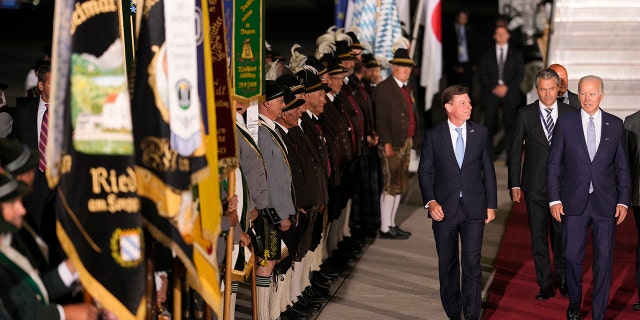 U.S. President Joe Biden, right, waves as he walks past Bavarian mountain riflemen and traditional costumers after his arrival at Franz-Josef-Strauss Airport near Munich, Germany, Saturday, June 25, 2022, ahead of the G7 summit. Biden is in Germany to attend a Group of Seven summit of leaders of the world's major industrialized nations. (AP Photo/Markus Schreiber)