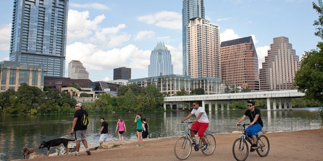 Cyclists pass beneath the downtown skyline on the hike and bike trail on Lady Bird Lake in Austin, Texas 