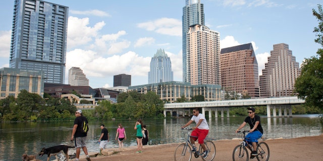 Cyclists pass beneath the downtown skyline on the hike and bike trail on Lady Bird Lake in Austin, Texas 