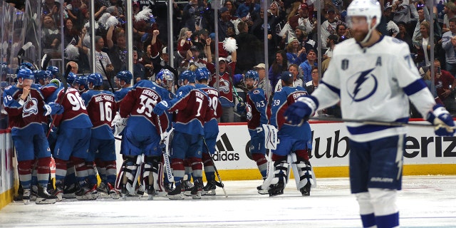 The Colorado Avalanche surround and celebrate with teammate Andre Burakovsky #95 in the corner after Burakovsky scored the game-winning goal in overtime as Victor Hedman, #77 of the Tampa Bay Lightning, skates toward the bench area in Game One of the 2022 Stanley Cup Final at Ball Arena on June 15, 2022 in Denver, Colorado. The Avalanche defeated the Lightning 4-3 in overtime.