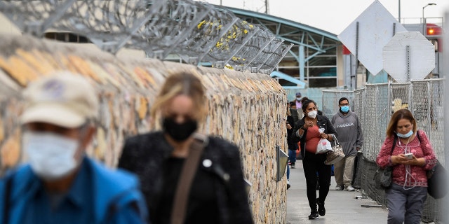 People walk along a fence after crossing the border from Mexico at the US Customs and Border Protection Paso del Norte Port of Entry along the US-Mexico border between Texas and Chihuahua state on December 9, 2021, in El Paso, Texas. 