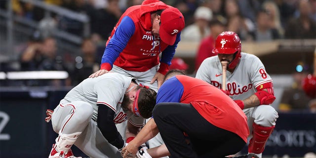 Philadelphia Phillies' Bryce Harper, left, receives attention after being hit by a pitch while interim manager Rob Thomson, background left, and Nick Castellanos, background right, look on during the fourth inning of the team's baseball game against the San Diego Padres, Saturday, June 25, 2022, in San Diego. 
