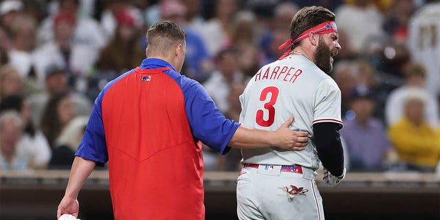Philadelphia Phillies' Bryce Harper, right, reacts towards San Diego Padres' Blake Snell after being hit by a pitch from Snell, as he walks off the field with a trainer during the fourth inning of a baseball game Saturday, June 25, 2022, in San Diego. 