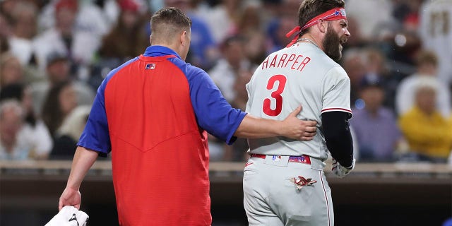 Philadelphia Phillies' Bryce Harper, right, reacts towards San Diego Padres' Blake Snell after being hit by a pitch from Snell, as he walks off the field with a trainer during the fourth inning of a baseball game Saturday, June 25, 2022, in San Diego.
