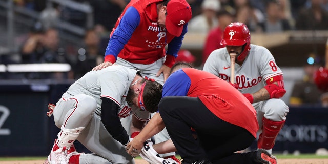 The Philadelphia Phillies' Bryce Harper, left, receives attention after being hit by a pitch while interim manager Rob Thomson, background left, and Nick Castellanos, background right, observe during the fourth inning of the team's game against the San Diego Padres, Saturday, June 25, 2022, in San Diego.