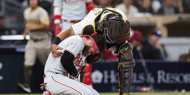 The Philadelphia Phillies' Bryce Harper, bottom, reacts after being hit by a pitch from San Diego Padres pitcher Blake Snell as Padres catcher Jorge Alfaro checks on him Saturday, 六月 25, 2022, 在圣地亚哥. 