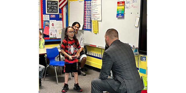 Proud father David Diaz Sr. (in back, left, behind his son) looks on as David Diaz Jr., 7, is presented with a New York State Senate Commendation Award in June 2022. 