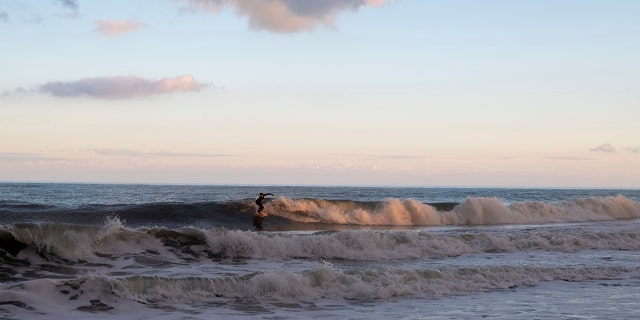 A surfer rides a wave at dusk in Rehoboth Beach, Delaware.