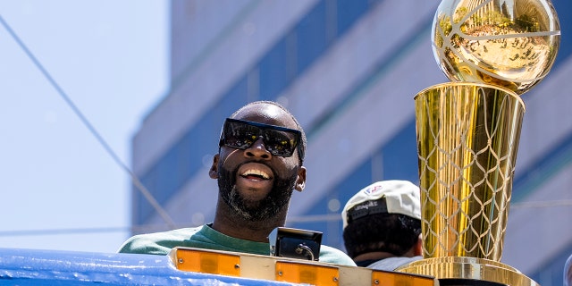 Golden State Warriors' Draymond Green stands next to the Larry O'Brien trophy during the NBA Championship parade in San Francisco, Monday, June 20, 2022, in San Francisco.