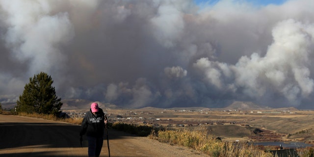FILE - A woman takes a walk before evacuating as smoke fills the sky as the East Troublesome Fire burns outside Granby, Colorado, Oct. 22, 2020.