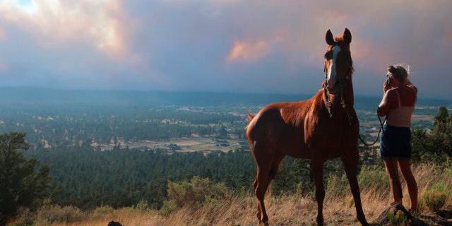 Janetta Kathleen and her horse, Squish, watch as smoke rises above neighborhoods on the outskirts of Flagstaff, Ariz., Sunday, June 12, casts a glow above neighborhoods. Evacuations have been ordered for homes in the area. Authorities say firefighters are responding to the wildfire about six miles north of Flagstaff that has forced evacuations.