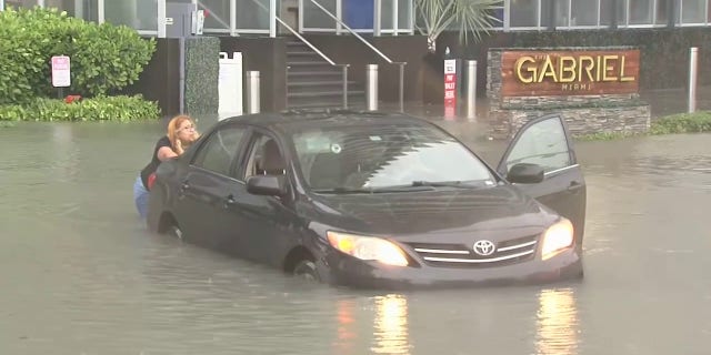A woman pushes her car that was stuck in floodwaters in Miami as a tropical depression swept over South Florida, Saturday, June 4, 2022.