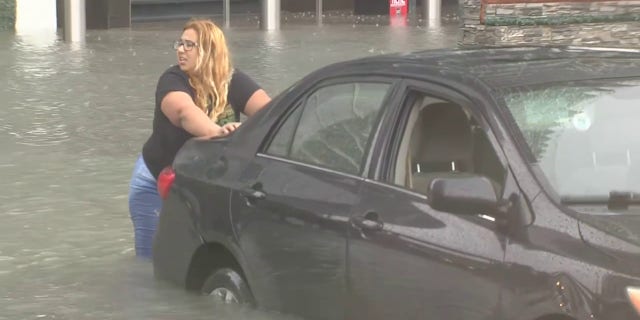 A woman pushes her car that was stuck in floodwaters in Miami as a tropical depression swept over South Florida, Saturday, June 4, 2022.