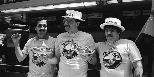 Three male contestants in the Nathan's Hot Dog Eating Contest in Coney Island, New York, pose with plates of hot dogs, circa July 4, 1987.