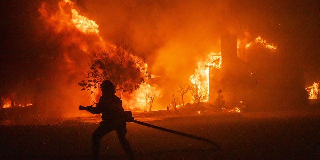Bloomberg Best of the Year 2020: A firefighter carries a hose as buildings burn in the Skyhawk Park neighborhood of East Santa Rosa during wildfires in Sonoma County, California, U.S., on Sunday, Sept. 27, 2020.