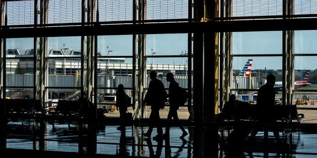 American Airlines aircrafts are seen in the background behind travelers passing through Ronald Reagan Washington National Airport in Arlington, Virginia on April 11, 2022. 