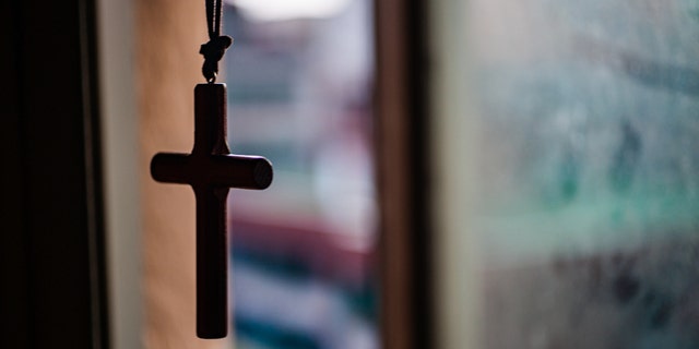 Cross necklace hanging in front of a window